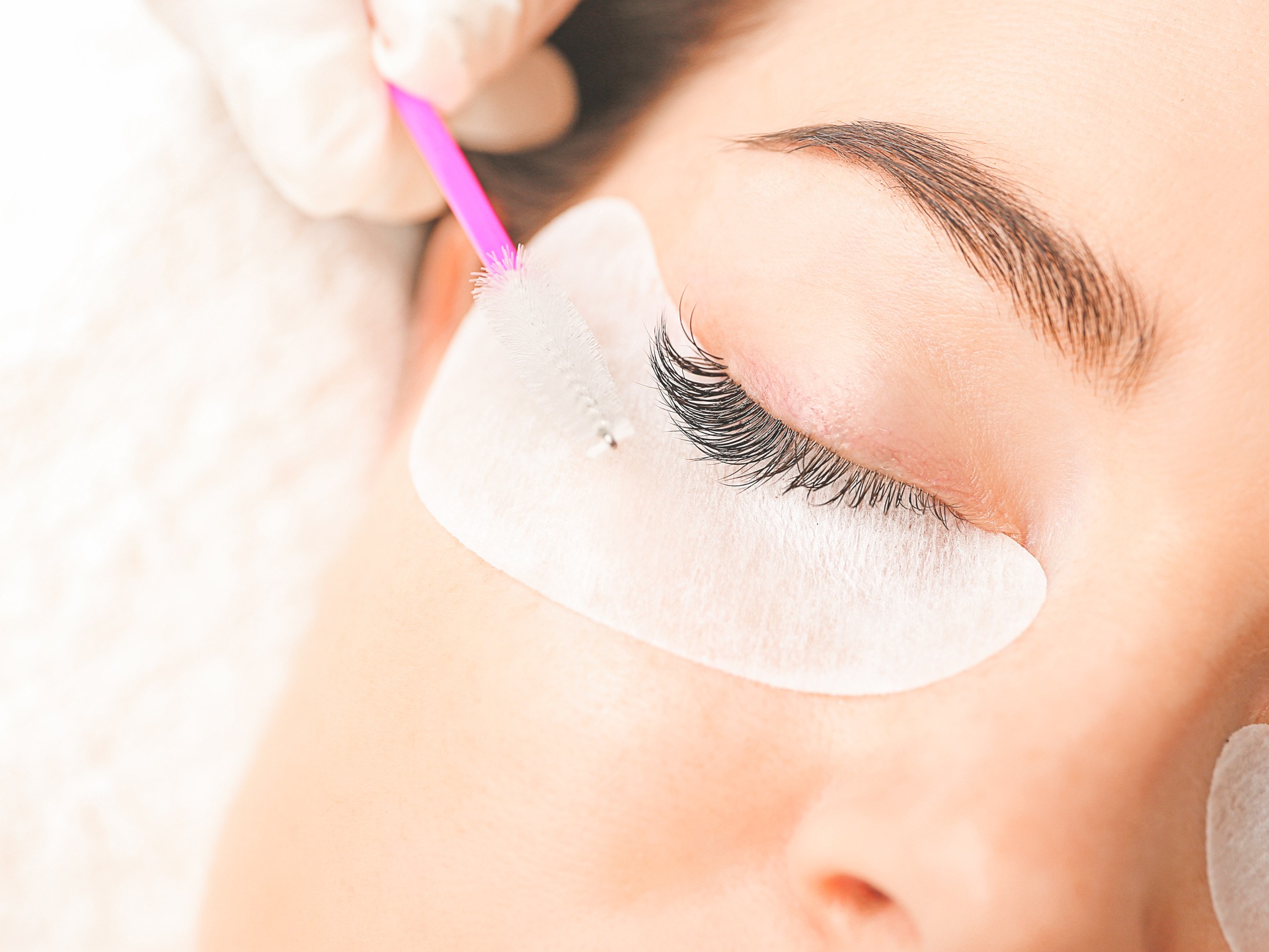Young woman undergoing eyelash extension procedure in beauty salon, closeup